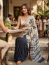 Woman in a saree sitting at an outdoor cafe table with other patrons in the background.