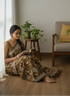 Woman in a patterned dress sitting on the floor reading a book in a cozy living room.