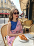 Woman sitting at a cafe table with a croissant and coffee, wearing sunglasses and a blue top with a pink saree.