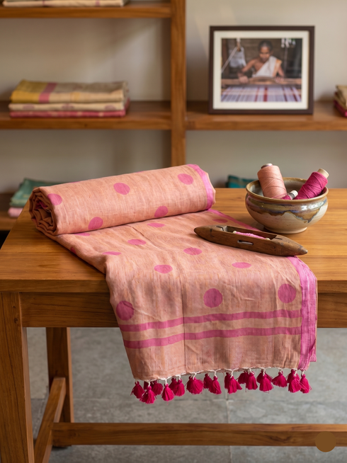 Pink and red patterned fabric with tassels on a wooden table, with books and a photo frame in the background.