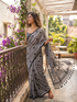 Woman in a gray saree with black polka dots on a balcony with flowers and greenery.
