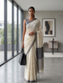 Woman in a beige saree with black patterns standing in a modern room.